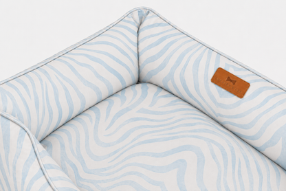 Close-up detail of a Chester & Lee luxury dog bed featuring a soft pastel blue and white zebra pattern, reinforced supportive bolsters, and the signature debossed leather brand patch