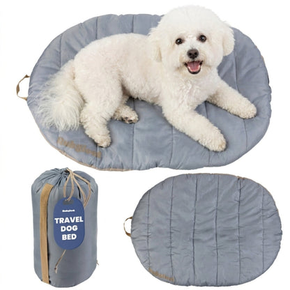 A fluffy white poodle mix lounging on a small grey Rubyloo roll-up travel dog bed paired with a compact cinch carry bag.
