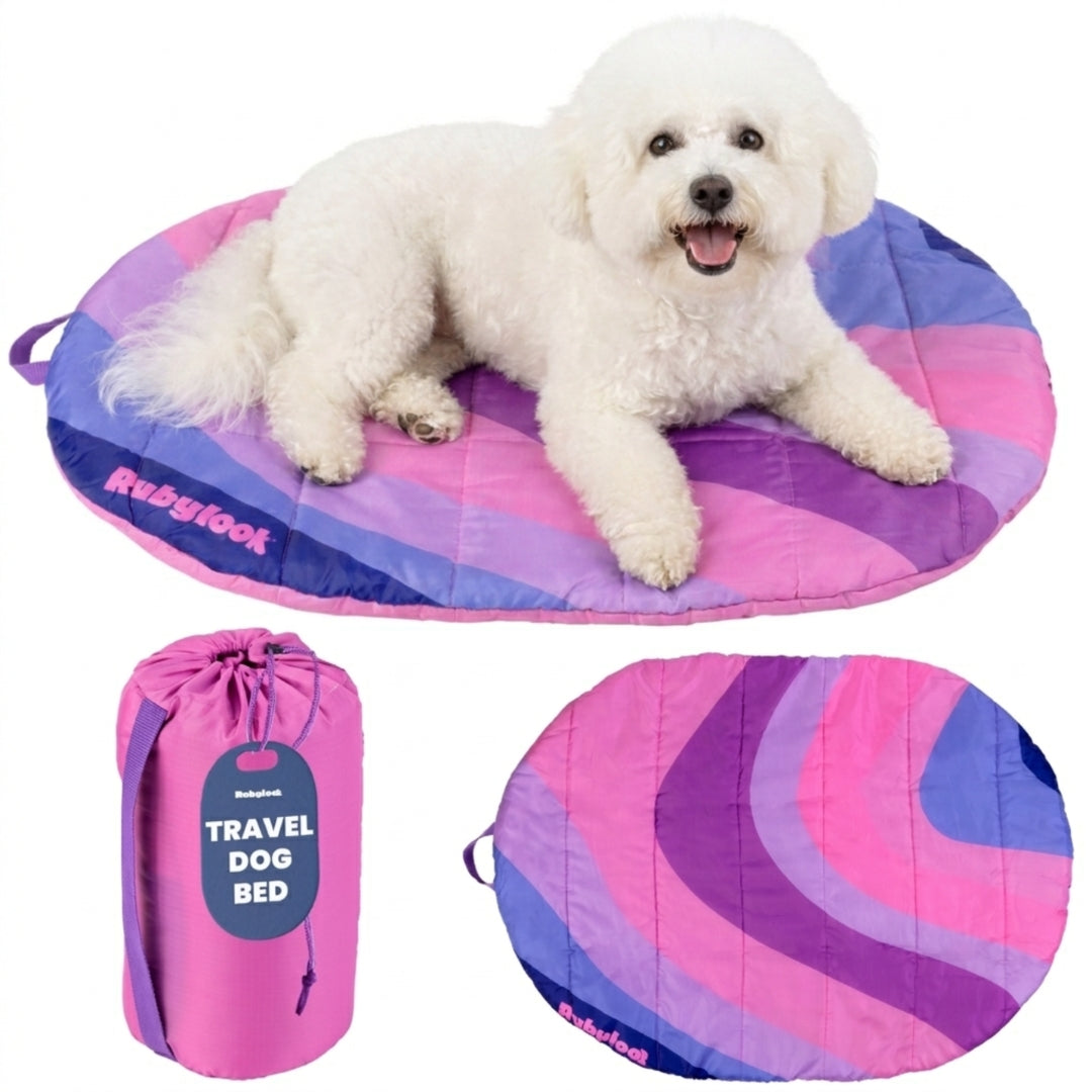 A fluffy white dog resting on a colorful teal and orange striped Rubyloo portable travel dog bed with a matching compression carry bag.