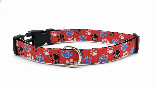 Red small dog collar with black, blue, and white paw print design and metal D-ring.
